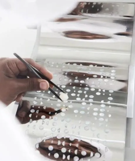 A hand placing pearl details with tweezers onto a reflective sheet