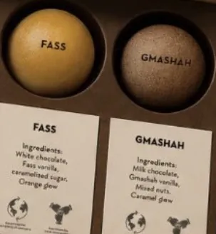 Two Chocolate Pearls in a gift box, Fass in golden white chocolate and Gmashah in speckled milk chocolate, each above its name card